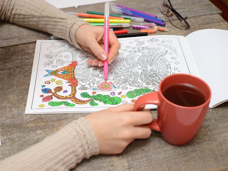 Woman coloring an adult coloring book and drinking tea